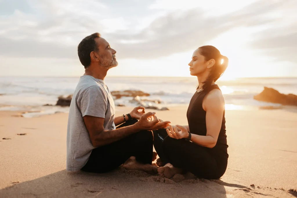 Two people balancing their chakra on the seashore of the beach.